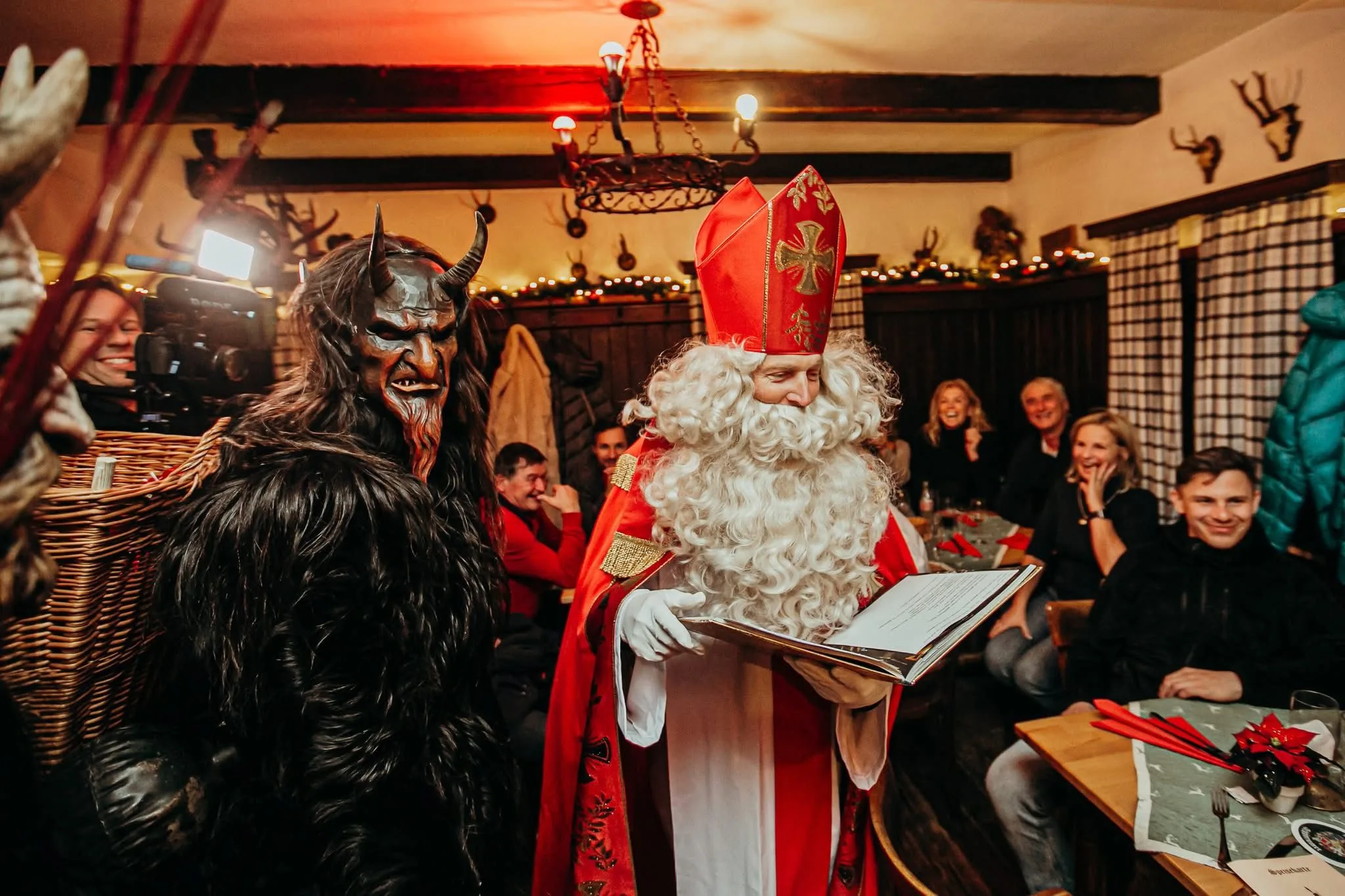 Ein Krampus mit Holzmaske und der Nikolaus in einer Gaststube